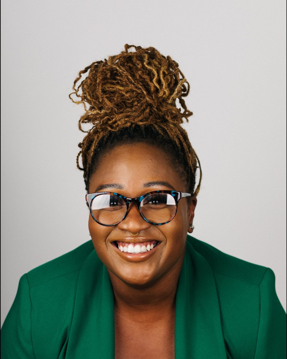 kenya, smiling, in tortoiseshell glasses and a green blazer